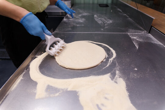 The cook processes the pizza dough with a special roller with spikes