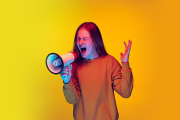 Half-length portrait of young emotive girl expressivelly shouting in megaphone isolated over yellow...