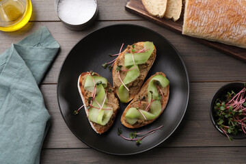 Slices of bread with delicious pate, cucumber and microgreens on wooden table, flat lay