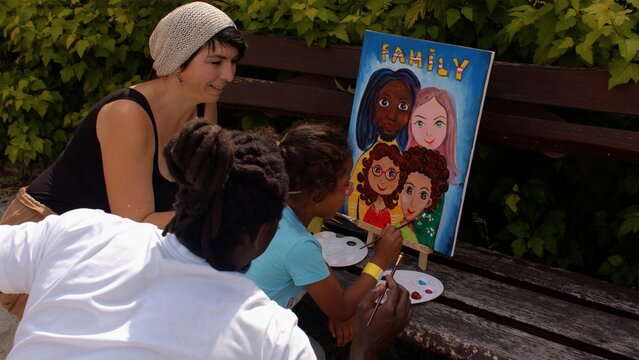 Sunny summer day for creative fantasy and creativity. Black man and caucasian woman with biracial girl paint a family portrait on canvas outdoor.