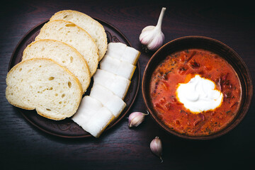 Traditional Ukrainian borscht, red vegetable and meat soup or borscht with sour cream on a wooden background. Slavic dish with cabbage, beets. Borscht on a dark background with bread and lard