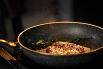 Close up view of preparation appetizing beef burger on grill with copy space. Frying and smoking juicy beef in pan with garlic and rosemary stick in restaurant kitchen . Concept of food.