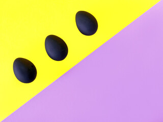 Black eggs on the yellow and violet background. Easter, diversity, geometric, pattern, food concept