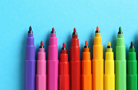 Many colorful markers on light blue background, flat lay. School stationery