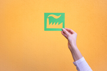 Hand holds green industry symbol on yellow background.