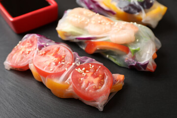 Delicious rolls wrapped in rice paper served on black table, closeup
