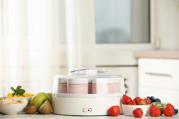 Modern yogurt maker with full jars and different fruits on white marble table indoors