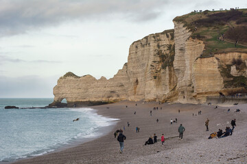 Falaises d'Etretat et minuscules touristes à leur pied. Plage de galet face à la mer et le...