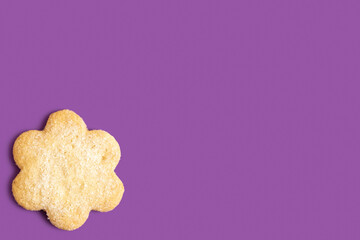 Butter cookie in the form of flower on purple background with copy space.
