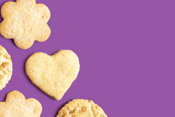 Butter cookies in the forms of heart and flower on purple background with copy space.