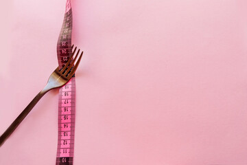 Fork  with measuring tape around on a pink background .Weight loss concept