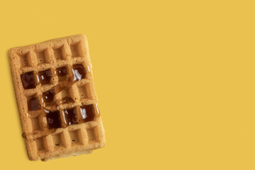 Waffle with maple syrup for International Waffle Day on yellow background with copy space.