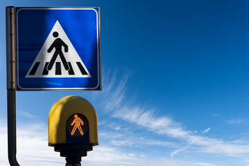 Close-up of a crosswalk sign and an orange pedestrian traffic light against a clear blue sky with...
