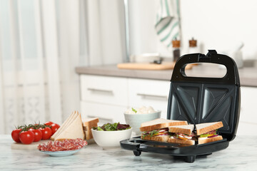 Modern grill maker with sandwiches and different products on white marble table in kitchen