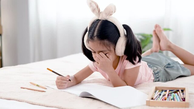 4K 50fps, adorable Asian girl tied her hair and wearing bunny ears, happily laying on a white bed drawing pictures..
