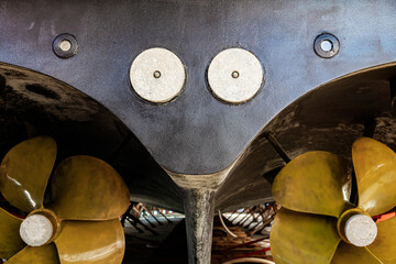 The back of a large motor yacht, standing on wooden blocks in a dry dock. Two propellers and zinc protective inserts. - obrazy, fototapety, plakaty