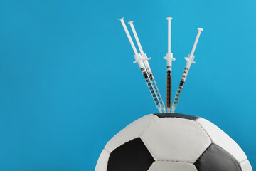 Closeup view of soccer ball with syringes on light blue background, space for text. Doping concept