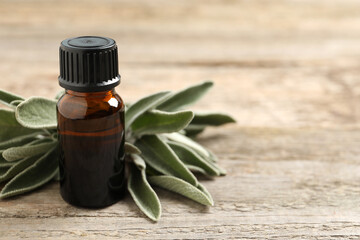 Bottle of essential sage oil and leaves on wooden table. Space for text