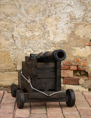 Fototapeta na wymiar Old cannon over stone wall. Old castle. Ancient cannon on wheels. Museum piece outdoor.