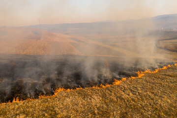 Aerial view of spring dry grass burning field. Fire and smoke in the meadow, nature pollution and danger,common waste are burned