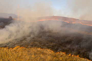 Aerial view of spring dry grass burning field. Fire and smoke in the meadow, nature pollution and danger,common waste are burned