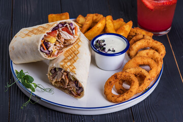 Shawarma and onion rings and garlic sauce on a black wooden background