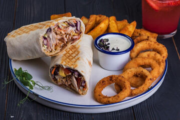 Shawarma and onion rings and garlic sauce on a black wooden background