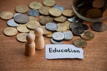 Education text on torn paper with jar, coins, wooden dolls and wooden table background. Education concept