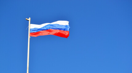 The flag of Russia is developing against a clear blue sky