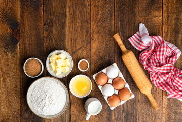 Baking ingredients on rustic wooden table background. Flour eggs sugar butter and rolling pin on brown wooden planks. Top view copy space