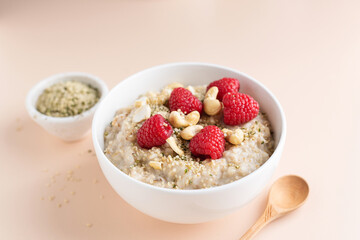 Oatmeal porridge with rasbperries, hemp seeds and cashews on beige background. Healthy breakfast food for dieting, weight loss