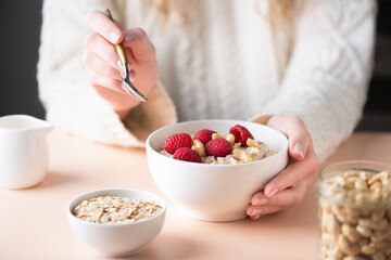 Young woman eating oatmeal porridge with raspberries. Healthy vegan nutritious breakfast cooked oatmeal in female hands - 494674486