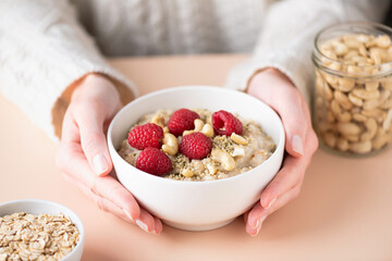 Oatmeal porridge with berries and seeds in caucasian female hands. Concept of eating healthy, vegan lifestyle, dieting