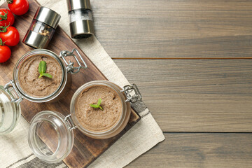 Glass jars with delicious liver pate on wooden table, top view. Space for text