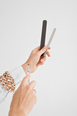 a woman's hand holds a nail file and manicure, manicure brush; a woman's hand in a white shirt holds manicure tools