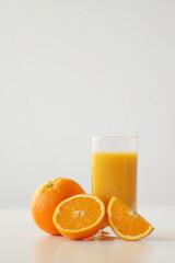 A whole orange, half and a quarter of an orange lie next to a glass of freshly squeezed orange juice. It is vitamin C, energy, cheerfulness and a good start to the day, an addition to breakfast