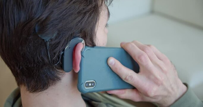 a man with a cochlear implant, with a hearing aid, speaks on a mobile phone at home