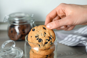 Woman taking delicious chocolate chip cookie from glass jar, closeup