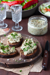 Lard on black bread on a wooden board with vodka in glasses, herbs and garlic