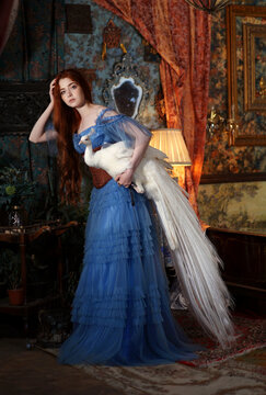 Girl in blue dress with white peacock in her arms in room with vintage interior