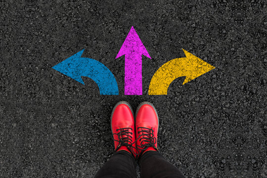 woman legs in boots standing on road with three direction arrow choices, left, right or move forward
