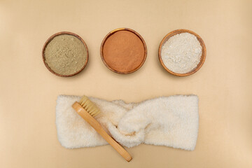Organic green, red, white clay for face mask with soft sponge bandage and bamboo and goat hair brush on beige background. Home skin care concept.Self care