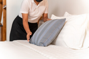 hand of maid setting up pillow on bed sheet in hotel room