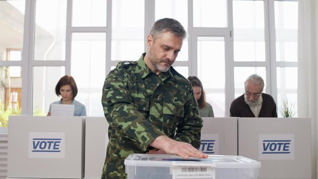Military man soldier putting voting ballot into box at polling place, elections