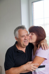 Fototapeta premium Elderly couple in casual clothes at light window of country house.