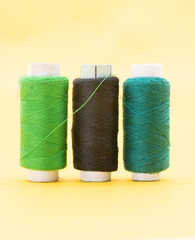 green,black and dark Cyan color yarn or spool thread over on yellow background