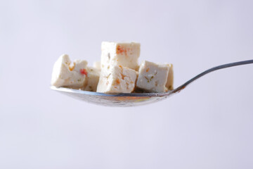 close up of fresh cheese cubes on a spoon on white background.