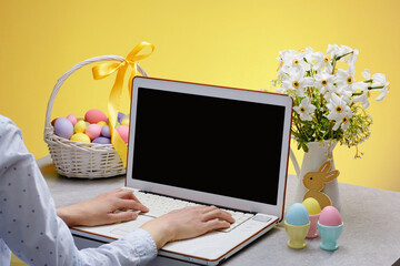 A laptop with a blank screen on a table festively decorated for the Easter holiday