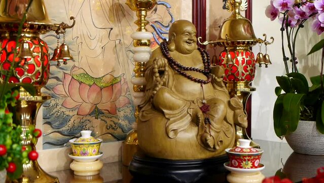 Wooden statue of laughing Buddha sitting on shrine filmed in panning motion