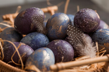 Purple, blue and golden eggs in a basket on a dark background. The purple hue trend of 2022 is very peri. Natural dye karkade tea. Top view. Easter card with a copy of the place for the text.